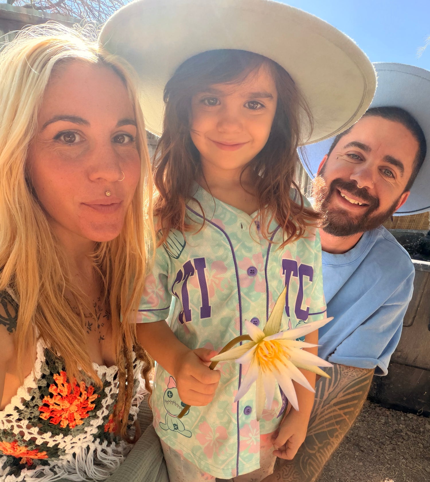 Two adults and a child holding a water lily flower outdoors on a sunny day.